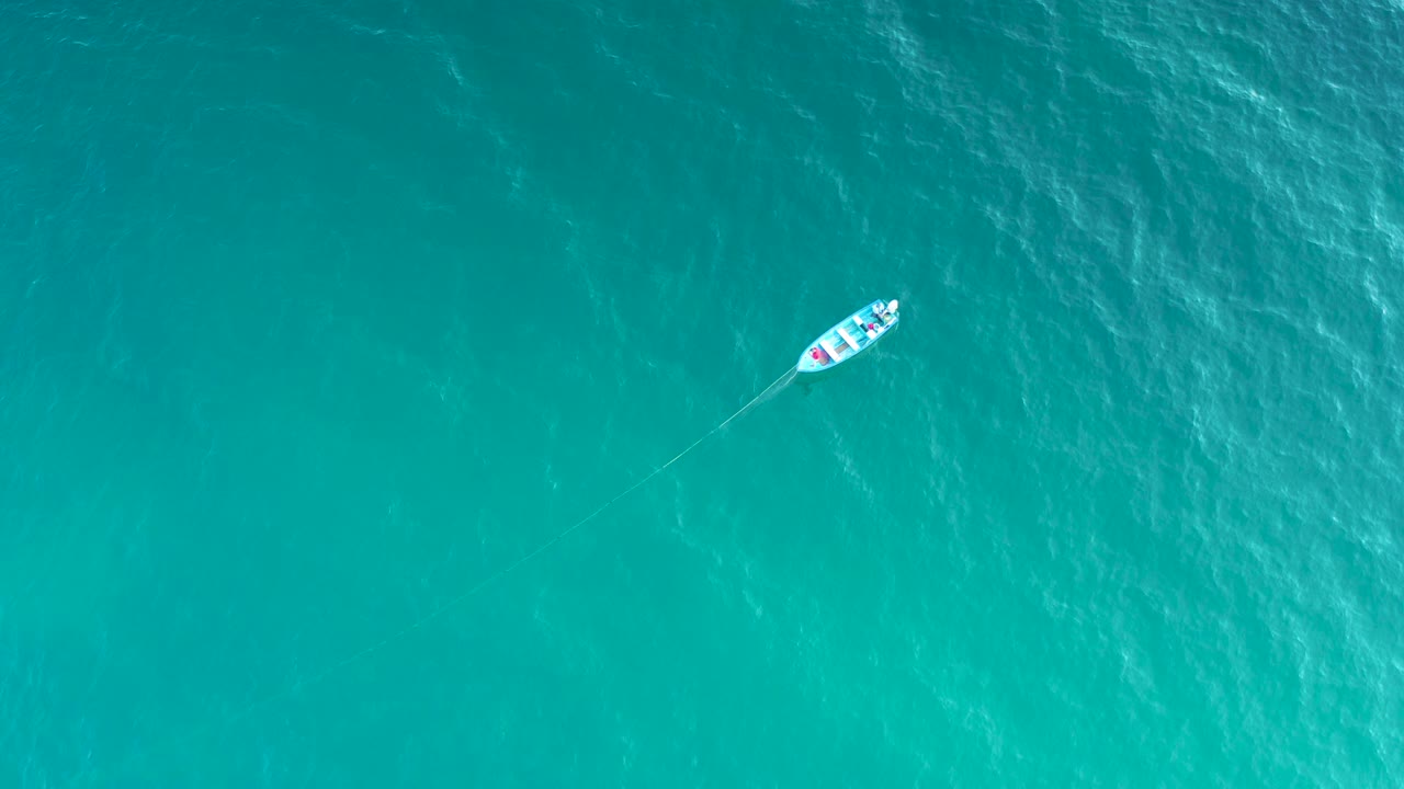 The boat appears near the upper right of the aerial frame, surrounded by turquoise ocean and faint white ripples in El Sargento La Ventana, Mexico, with no visible people.