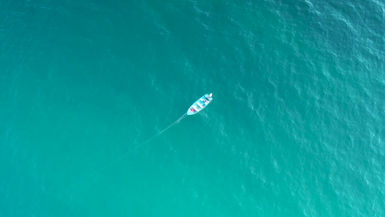 Overhead view of a small boat near the upper right of the frame over textured turquoise water in El Sargento La Ventana, Mexico, with no visible people.