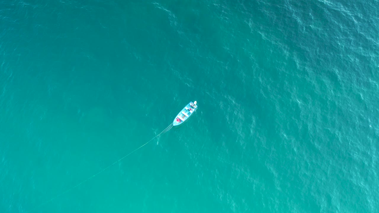 Aerial view of a small white boat near the upper left of bright turquoise water in El Sargento La Ventana, Mexico, with no visible people.