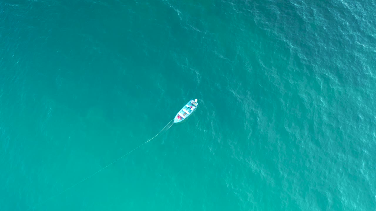A small white vessel sits high in the frame over textured turquoise sea in El Sargento La Ventana, Mexico, with no visible people.