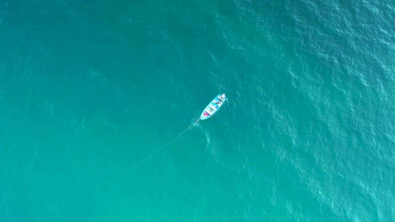 Overhead view in El Sargento La Ventana, Mexico, showing a small white boat near the upper left of clear aqua water with faint wake and no visible people.