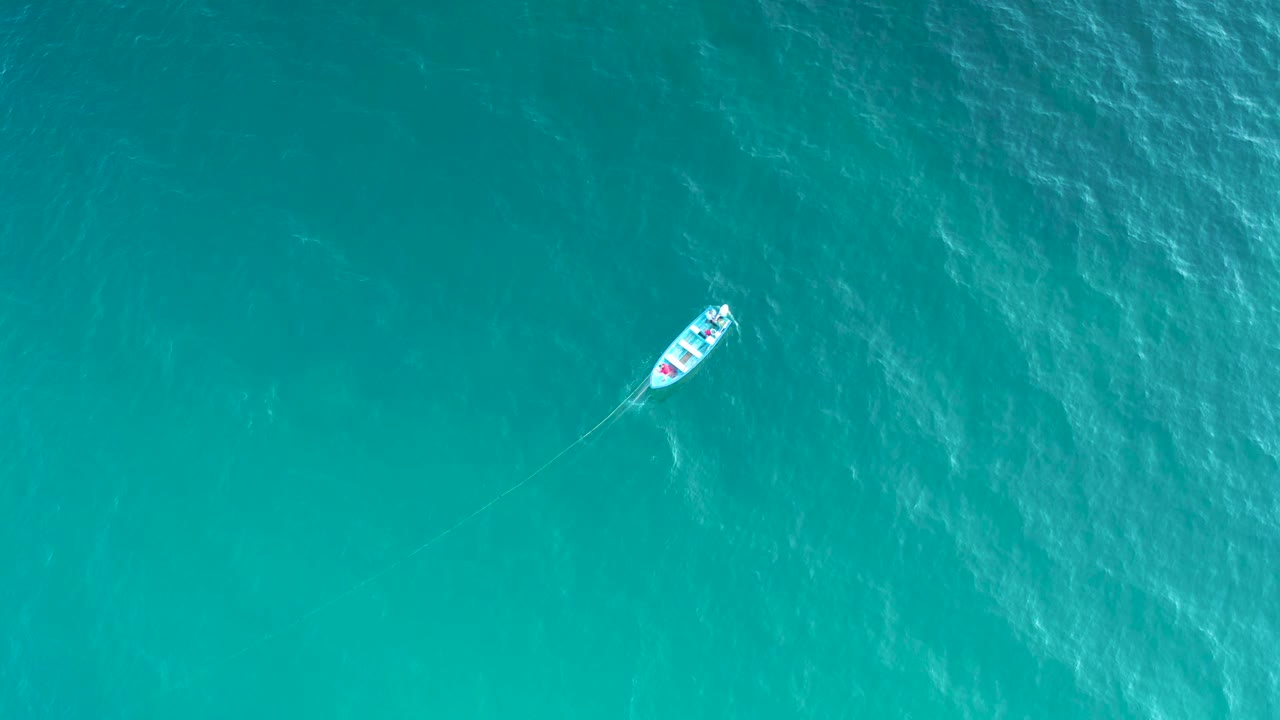 A high overhead frame in El Sargento La Ventana, Mexico, shows the white boat slightly farther across rippled blue-green water with no shoreline and no visible people.