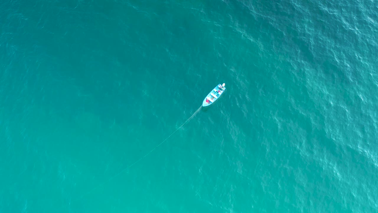A small boat sits high in the frame over textured blue-green sea in El Sargento La Ventana, Mexico, with a faint trailing line and no visible people.