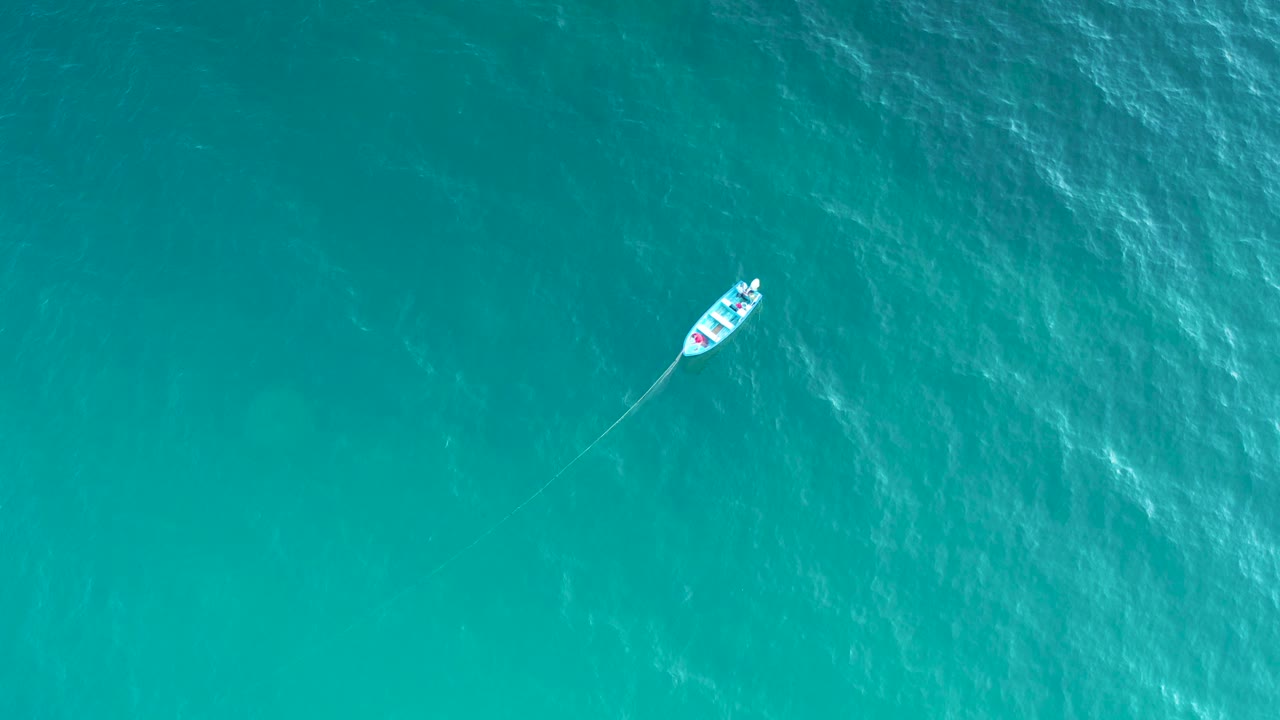 Small boat and trailing line on blue sea.