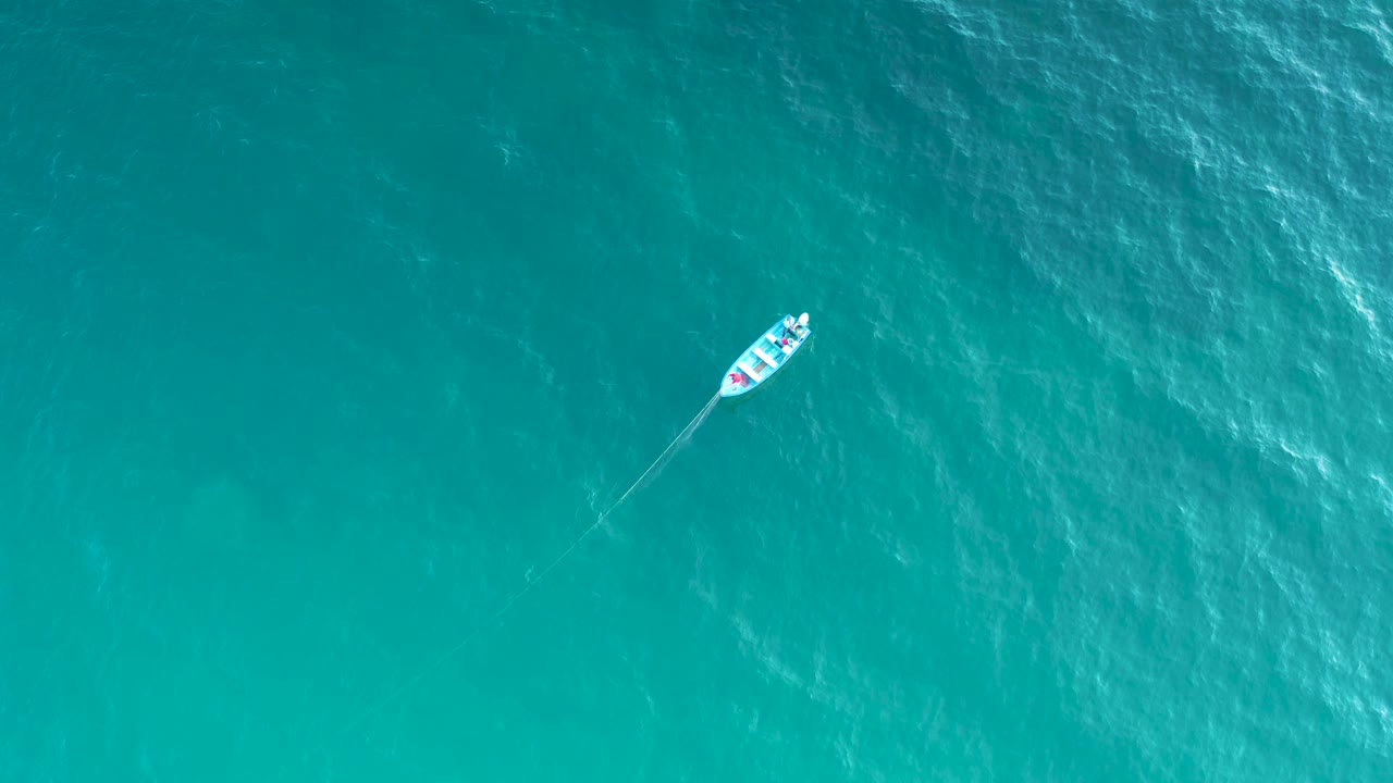 Aerial view with the boat near the top right over turquoise water, surrounded by uneven bright ripples and no visible people.