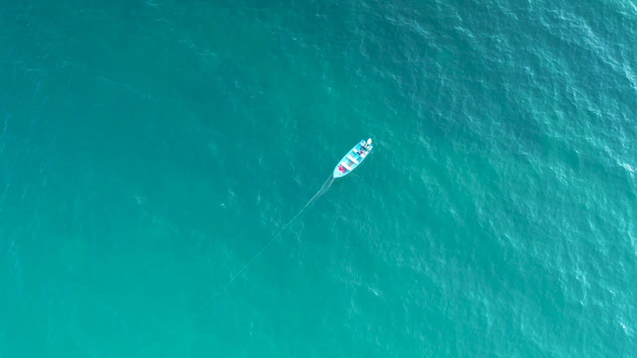 Small white boat on turquoise water from above