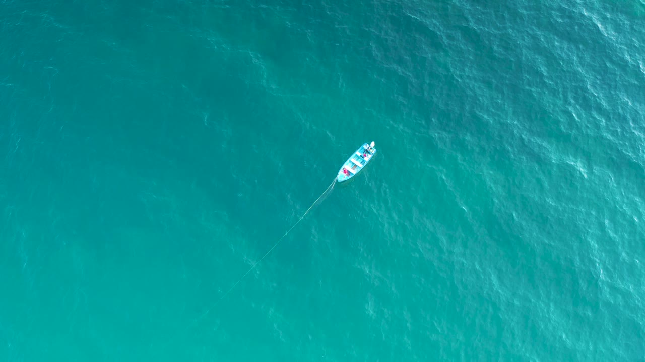 Aerial top-down frame of the small white boat near the upper right area of turquoise sea in El Sargento La Ventana, Mexico, with no shoreline and no visible people.