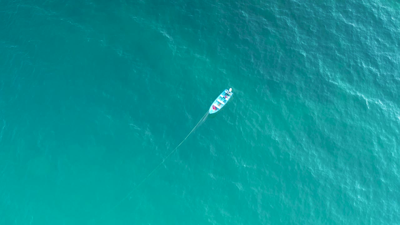 Overhead frame of the white boat moving across blue water in El Sargento La Ventana, Mexico, with brighter ripples crossing the sea surface and no visible people.