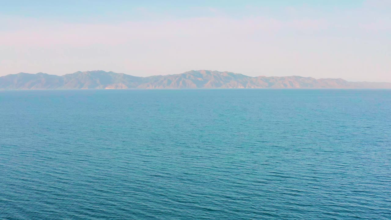 Second frame holds on calm open water with fine ripples leading to low tan-gray mountains in El Sargento La Ventana, Mexico, and no visible people.