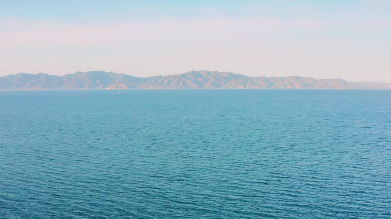 Wide view of blue sea texture and a hazy mountain ridge across the horizon in El Sargento La Ventana, Mexico, with no boats or visible people.