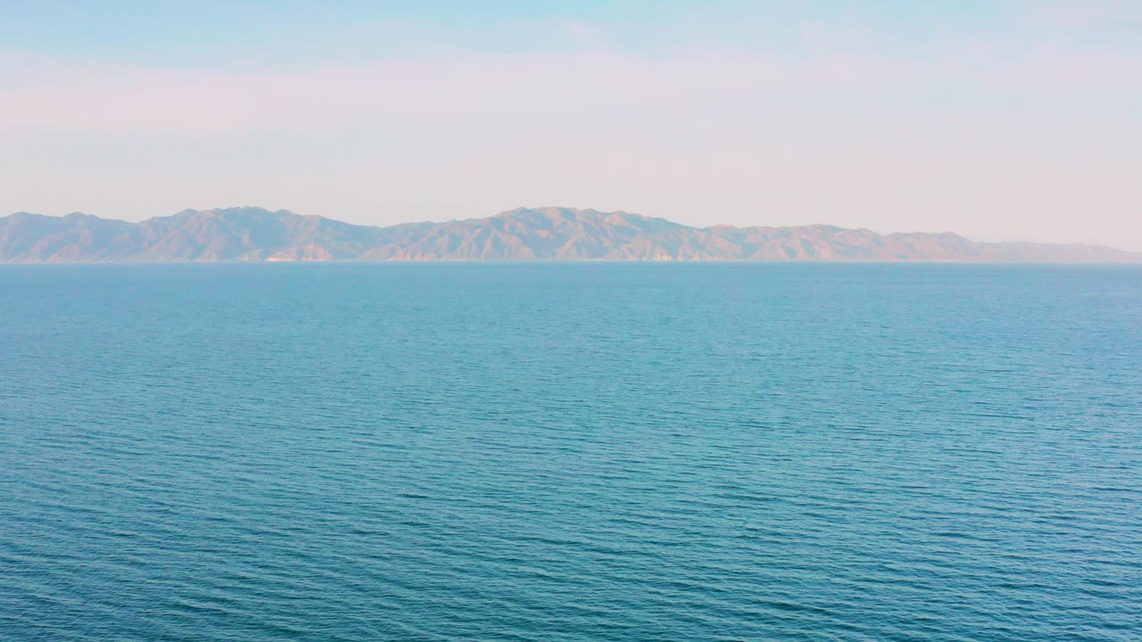 Opening frame of blue sea off El Sargento La Ventana, Mexico with a distant mountain ridge on the horizon and no visible people.