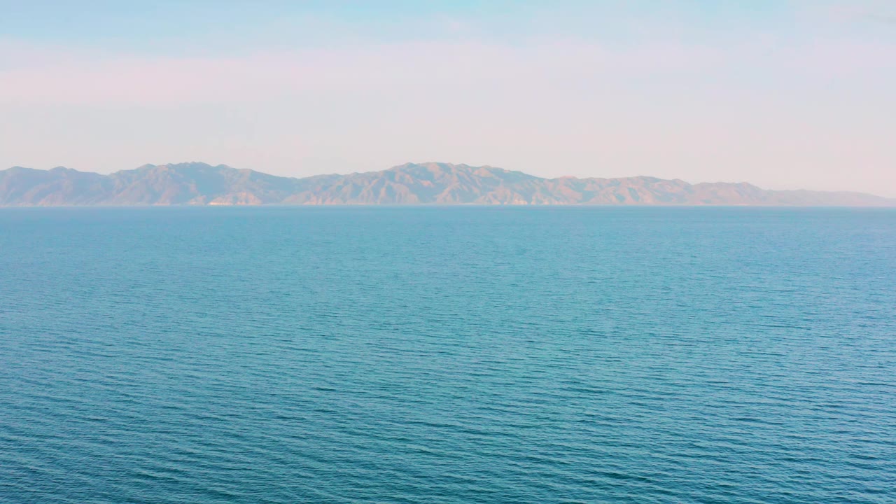 Blue open water fills the frame with low ripples, a hazy mountain ridge in the background, and no visible people at 0:01.