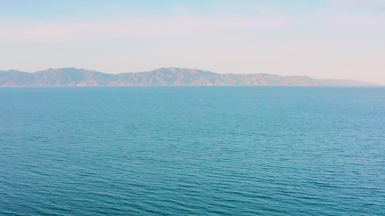 Pale sky over calm ocean and low coastal mountains