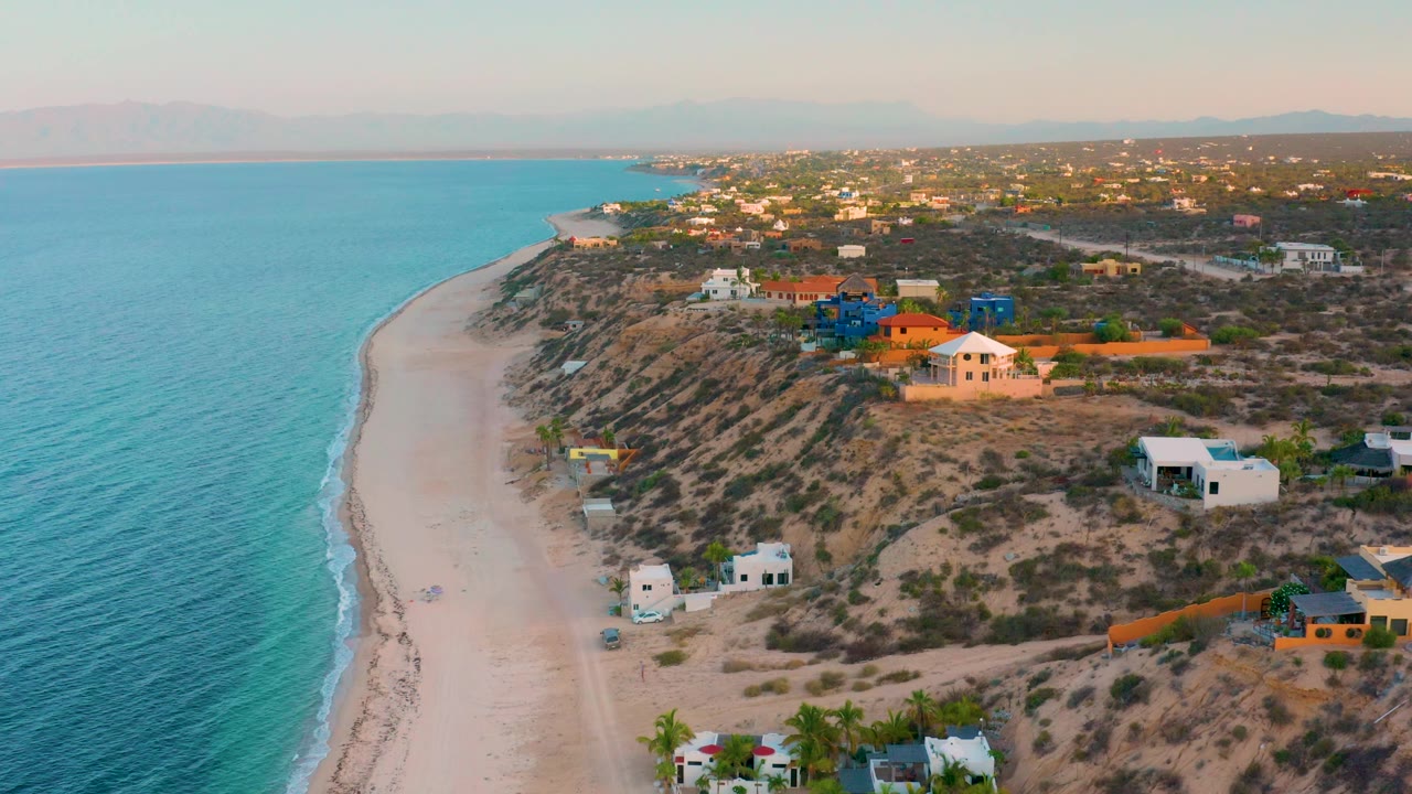 Aerial view along a quiet beach with houses and scrubland above.