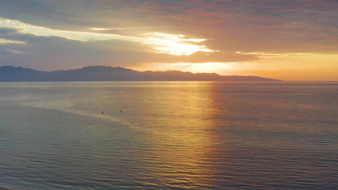 At 0:01, the bright reflection widens on the water as layered clouds sit above the mountain horizon in El Sargento La Ventana, Mexico, with no visible people.