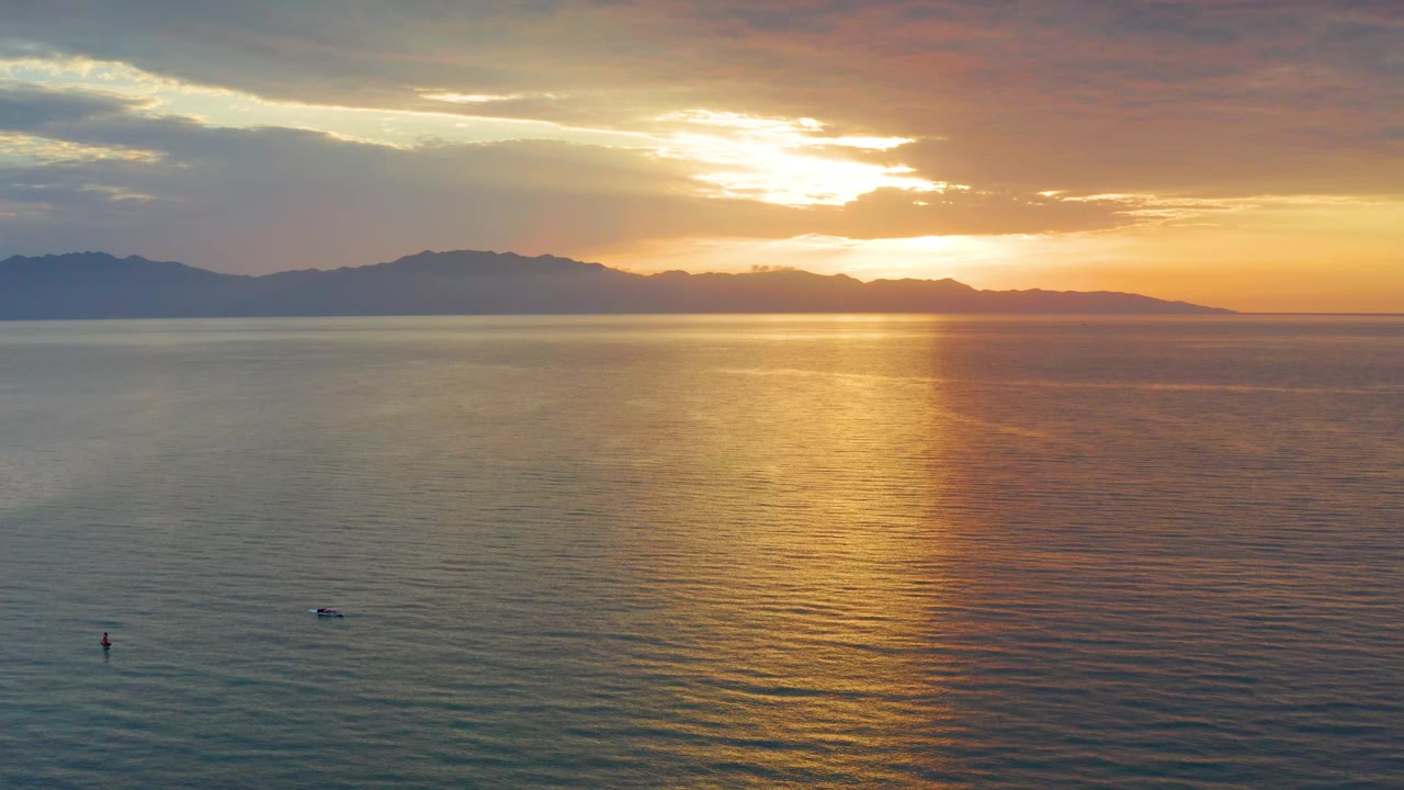At 0:02, orange light intensifies near the horizon as the sea stays darker in the foreground and the mountain ridge spans the background in El Sargento La Ventana, with no visible people.