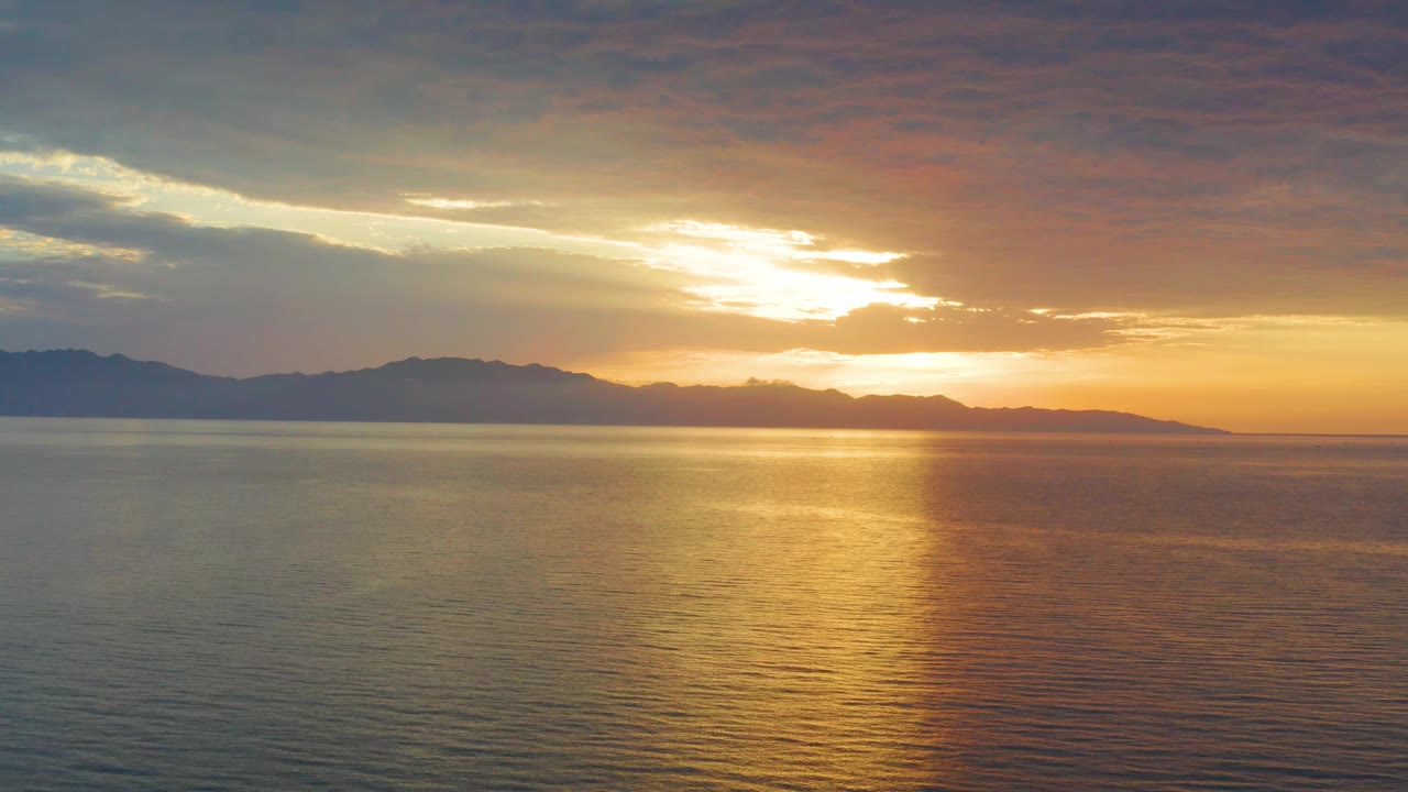 Mid-clip frame of the El Sargento La Ventana, Mexico sunset, with the mountain silhouette stretching farther across the horizon and a softer golden reflection spread over rippled water, with no visible people.