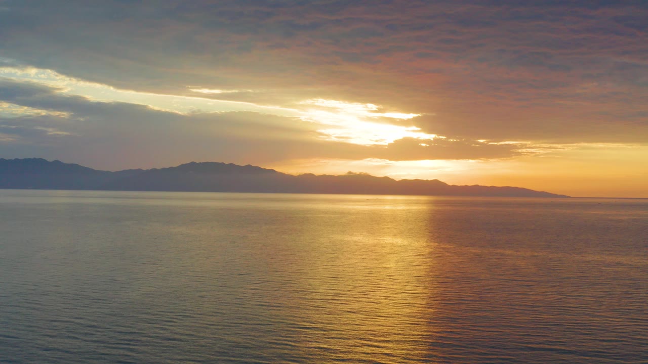 Opening frame of a sunset over the sea in El Sargento La Ventana, Mexico, with a bright gold reflection on rippled water and no visible people.
