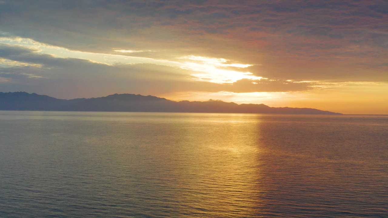 Opening frame from El Sargento La Ventana, Mexico, showing rippled water below a low sun, distant mountain silhouettes, layered clouds, and no visible people.