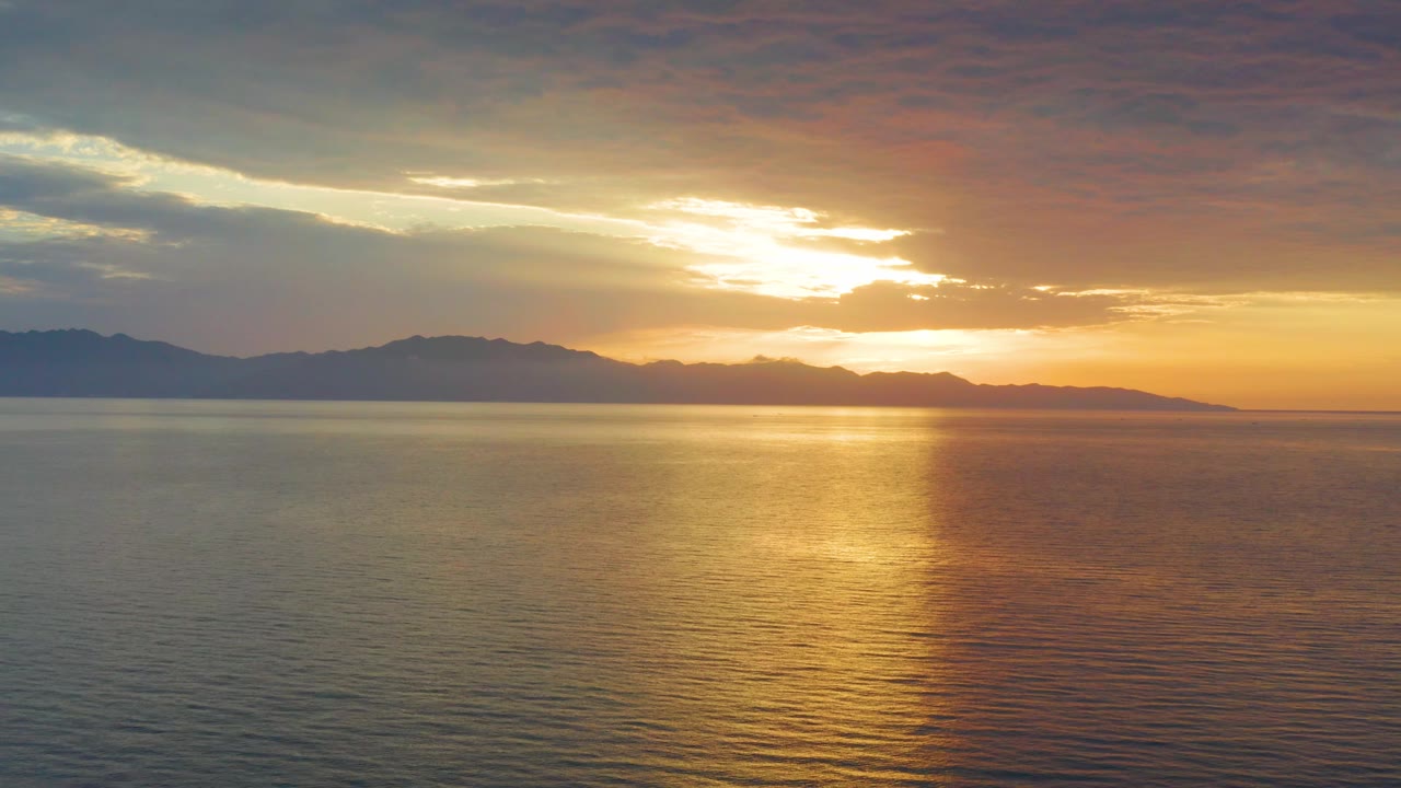 Cloudy sunset above calm water and dark mountain ridge