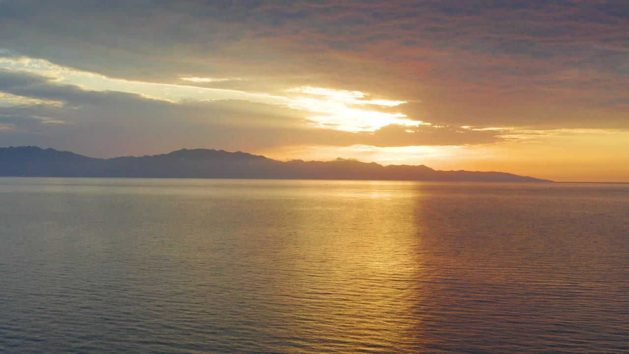 Golden sunset over rippled ocean water in El Sargento La Ventana, Mexico, with dark mountains along the horizon and no visible people.