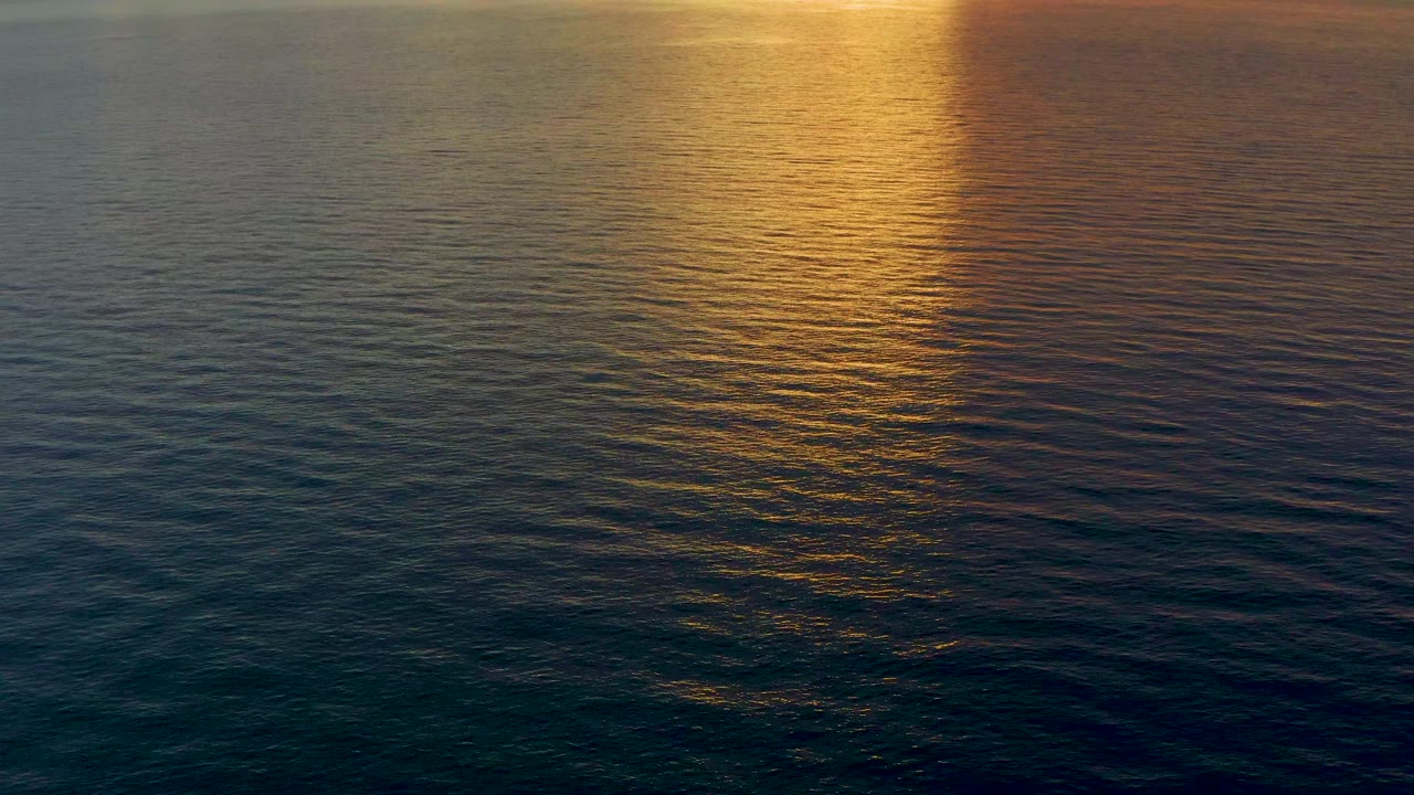 Warm orange and gold sunset light reflects on open ocean water in El Sargento La Ventana, Mexico, with subtle wave lines and no visible people.