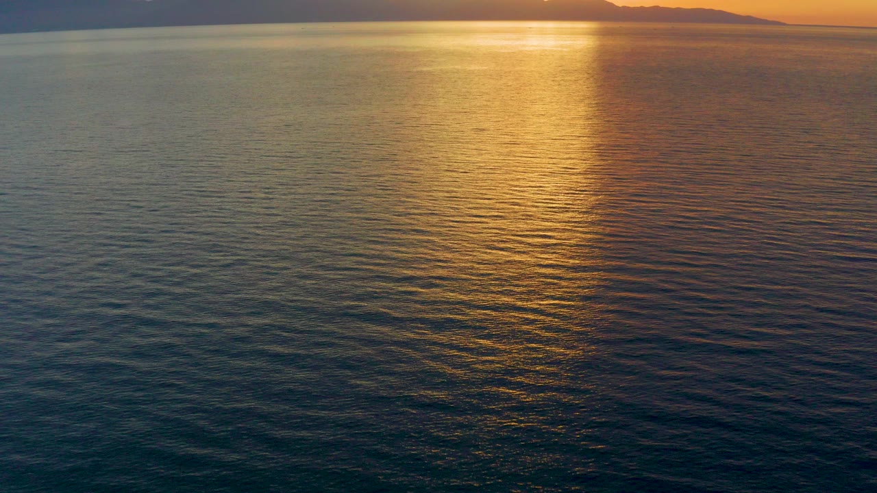 Opening frame over El Sargento La Ventana water, with a gold sunset reflection stretching down rippled ocean toward the camera and no visible people.