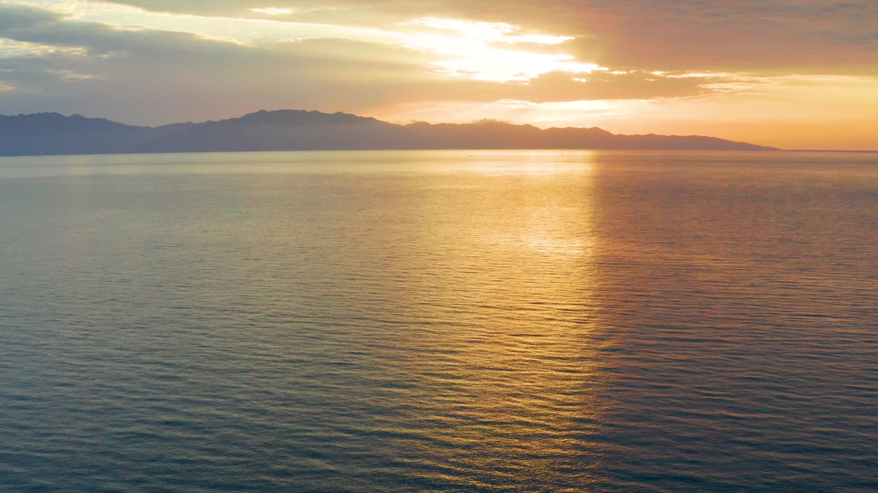 Opening frame of an El Sargento La Ventana, Mexico sunset over rippled sea, with a dark mountain skyline under layered clouds and no visible people.
