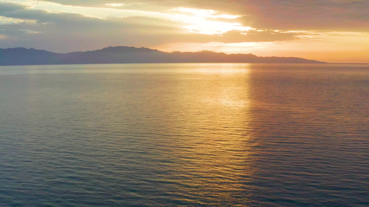 One second in, the sun glow sits behind broken clouds over El Sargento La Ventana, Mexico, casting a broad gold path on the sea with no visible people.