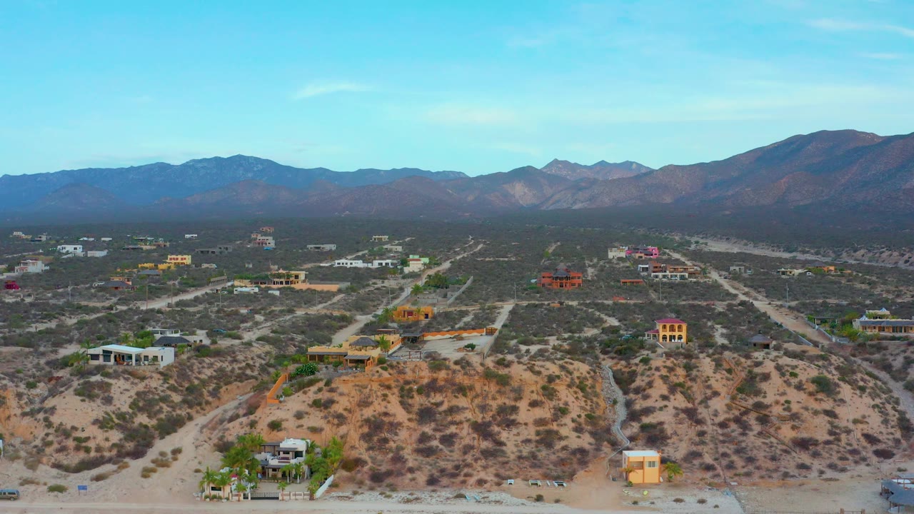 High aerial frame of El Sargento La Ventana, Mexico, with sparse houses, branching dirt roads, scrub-covered lots, a broad mountain backdrop, and no visible people.