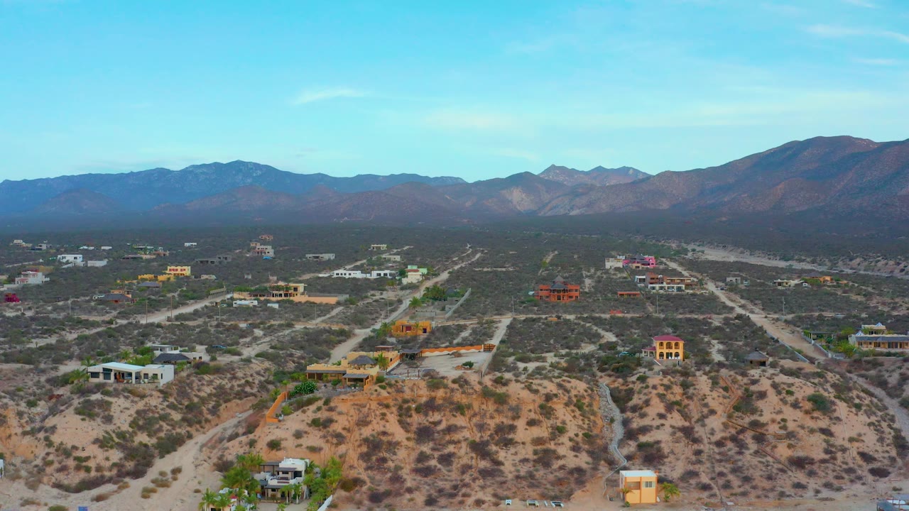 Aerial frame with tan hills, colorful buildings, dry roads, and distant mountains.