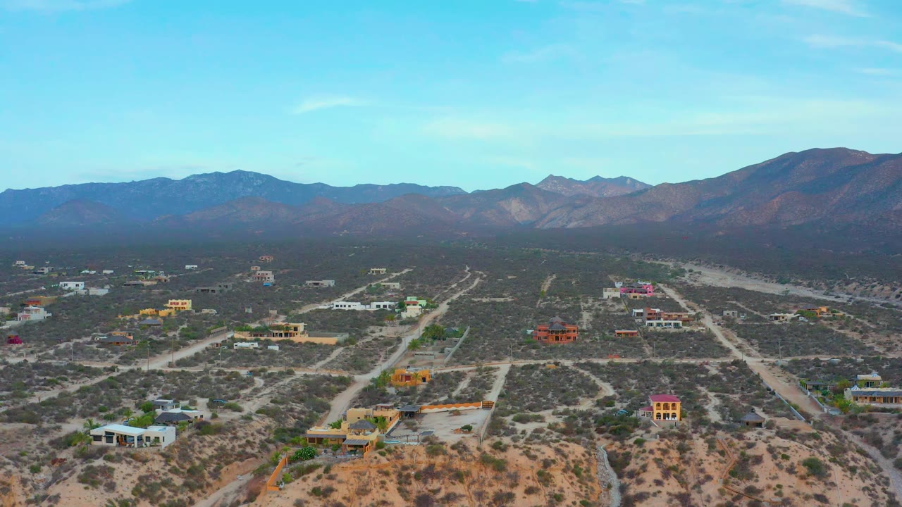 Aerial view in El Sargento La Ventana, Mexico, with low houses spread across brushy terrain, dirt tracks leading toward distant mountains, and no visible people.