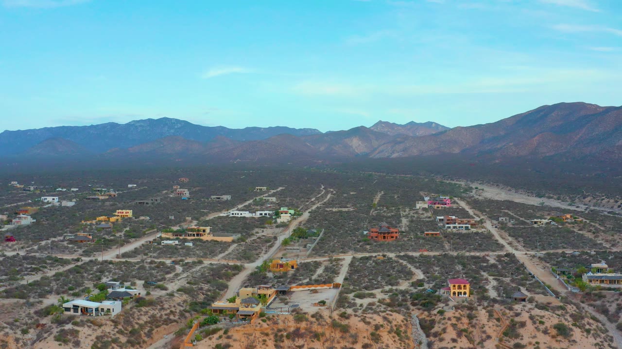 Wide drone-like frame over El Sargento La Ventana, Mexico, showing a loose grid of dirt roads, scattered homes, desert vegetation, mountains, and no visible people.