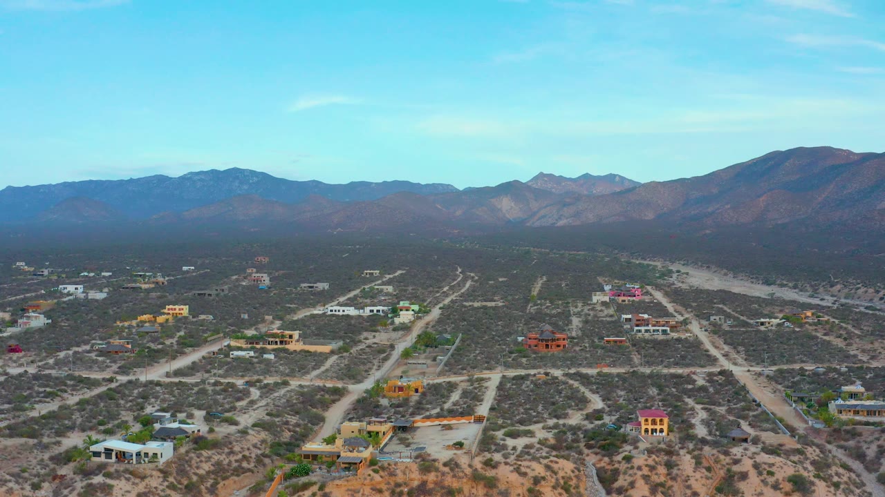 Aerial view of colorful houses and dirt roads across dry terrain below mountains.