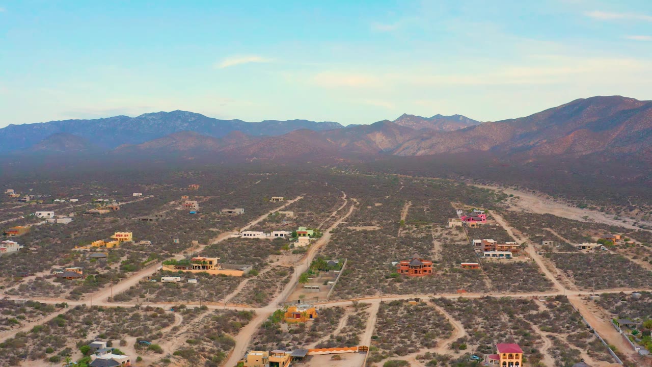 Wide overhead view of scrubland, dirt road grid, houses, and mountains