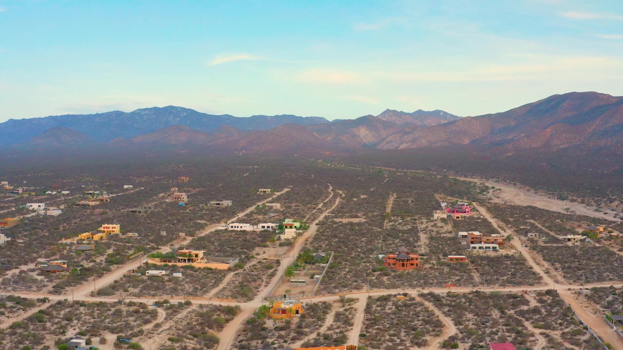 High view across arid lots, dirt tracks, houses, and mountains