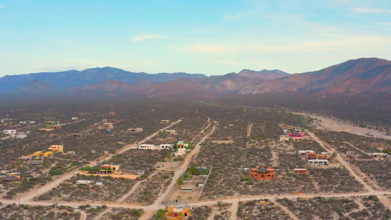 Opening aerial frame over El Sargento La Ventana, Mexico, with dirt roads, scattered homes, scrubland, distant mountains, and no visible people.