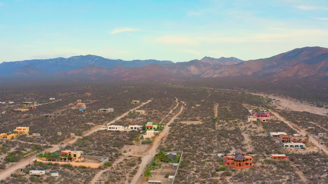 Aerial view of El Sargento La Ventana with small buildings in the foreground, open desert lots through the center, hazy mountains behind, and no visible people.