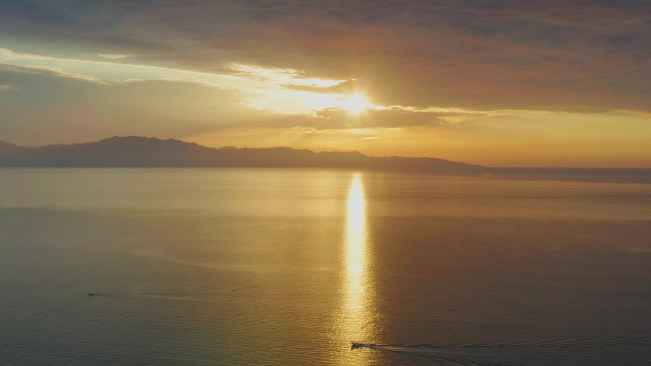 The sun sits partly behind clouds above the calm ocean in El Sargento La Ventana, Mexico, with the reflection centered lower in frame and no visible people.