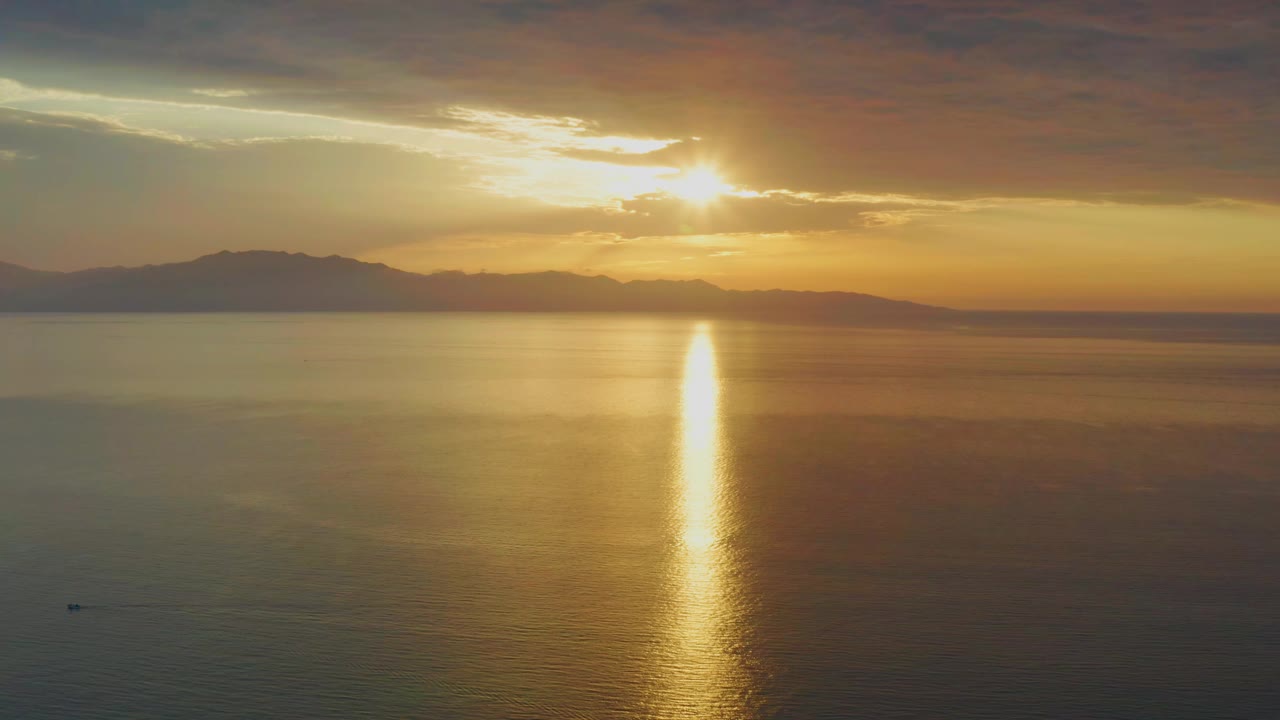 A wide sunset frame shows the sun breaking through clouds above open water in El Sargento La Ventana, Mexico, with a long gold streak running down the ocean and no visible people.