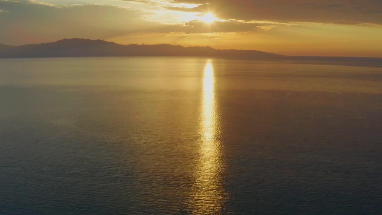 At 0:02, the reflection appears slightly farther right in the frame, while the distant mountains stretch under orange cloud cover in El Sargento La Ventana, Mexico, with no visible people.
