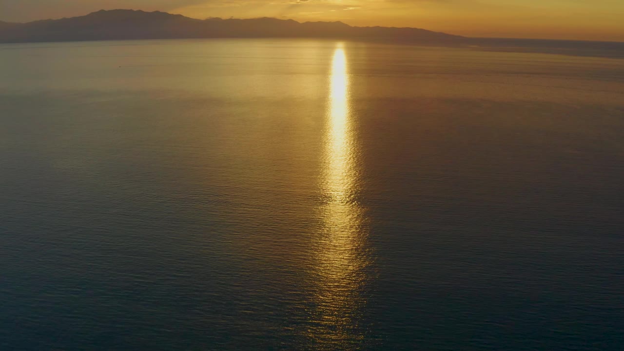 At 0:02, warm orange light spreads along the upper sky while the sun's gold reflection cuts down the open sea off El Sargento La Ventana, Mexico, with no visible people.