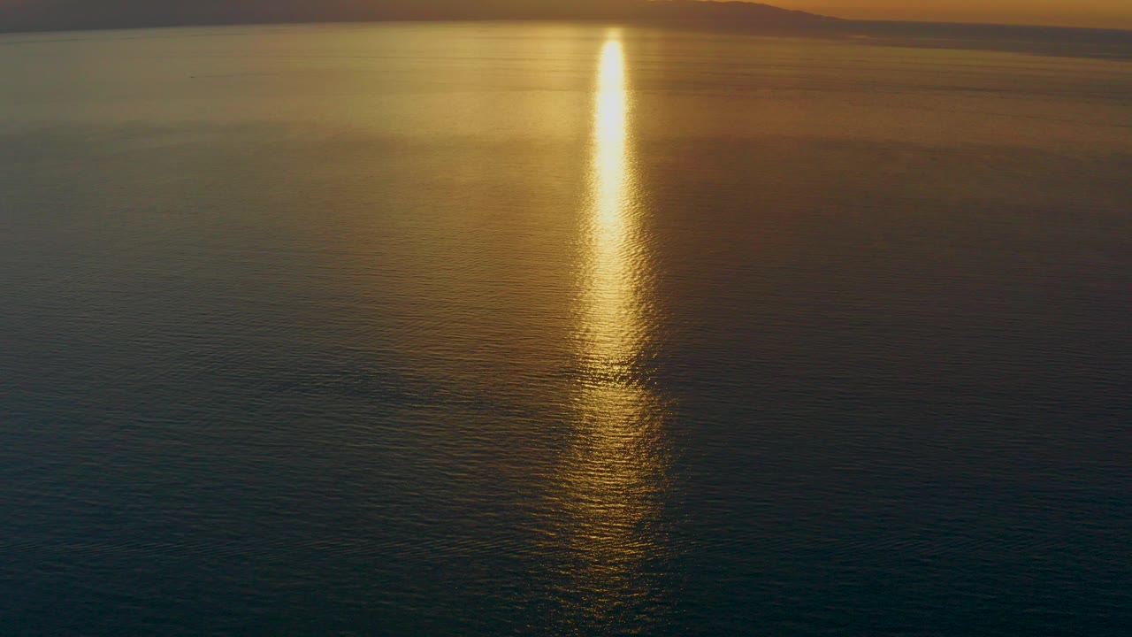 Warm sun reflection runs vertically across rippled water near El Sargento La Ventana, Mexico, with a faint distant shoreline at the top and no visible people.