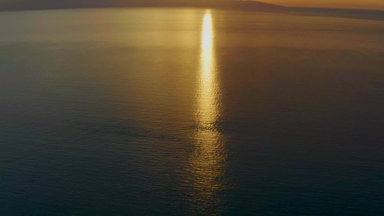 A bright golden column of reflected sunlight sits over dark blue ocean water near El Sargento La Ventana, Mexico, with soft amber tones and no visible people.