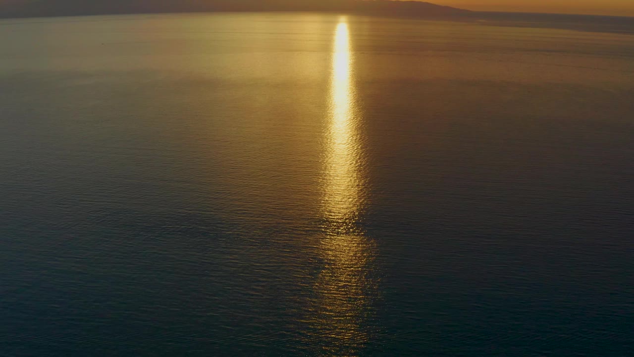 A vertical morning reflection crosses open water near El Sargento La Ventana, Mexico, with the upper sea reading warmer and the lower sea darker, and no visible people.