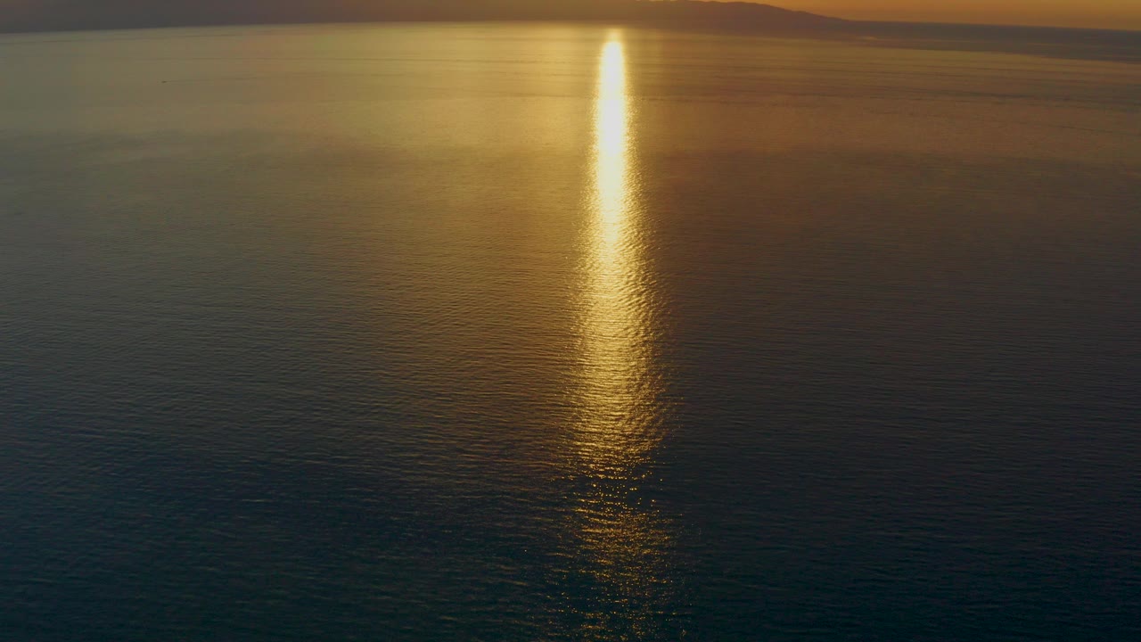 Opening frame of El Sargento La Ventana water at sunset, with a bright vertical sun path on dark ripples, distant mountain silhouettes, and no visible people.