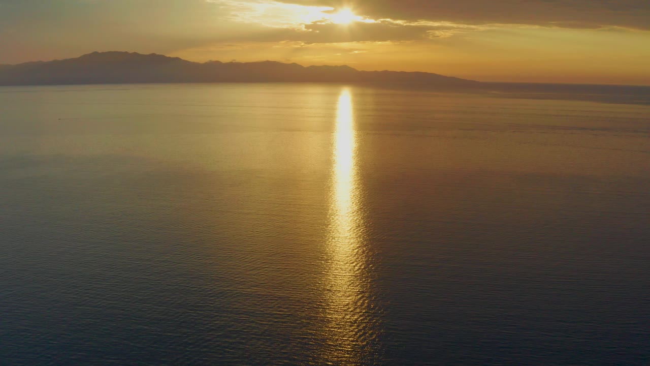 Early frame of El Sargento La Ventana, Mexico, showing low golden sun above distant mountains, a bright reflection on calm sea, and no visible people.