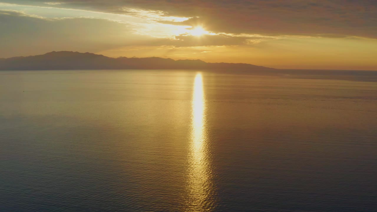 The sun sits above the mountain horizon in El Sargento La Ventana, Mexico, sending a narrow gold reflection down the calm water with no visible people.