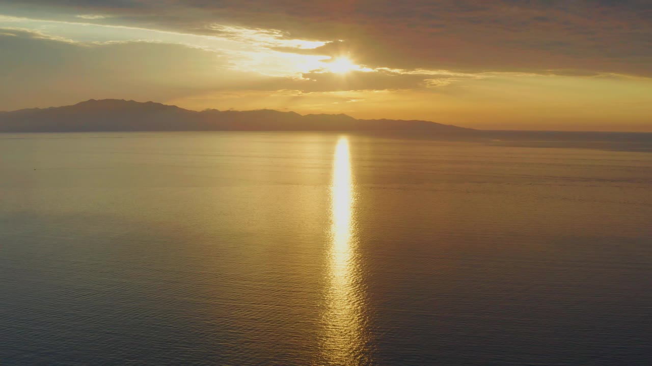 In El Sargento La Ventana, Mexico, the sun breaks through cloud cover above the horizon and reflects in a bright vertical streak on still water with no visible people.