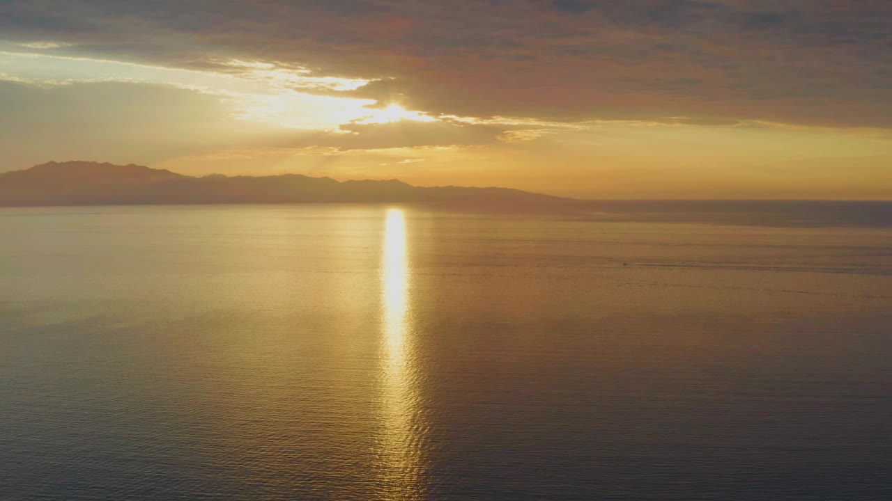 Sunlit water with mountain silhouette beneath dark clouds.